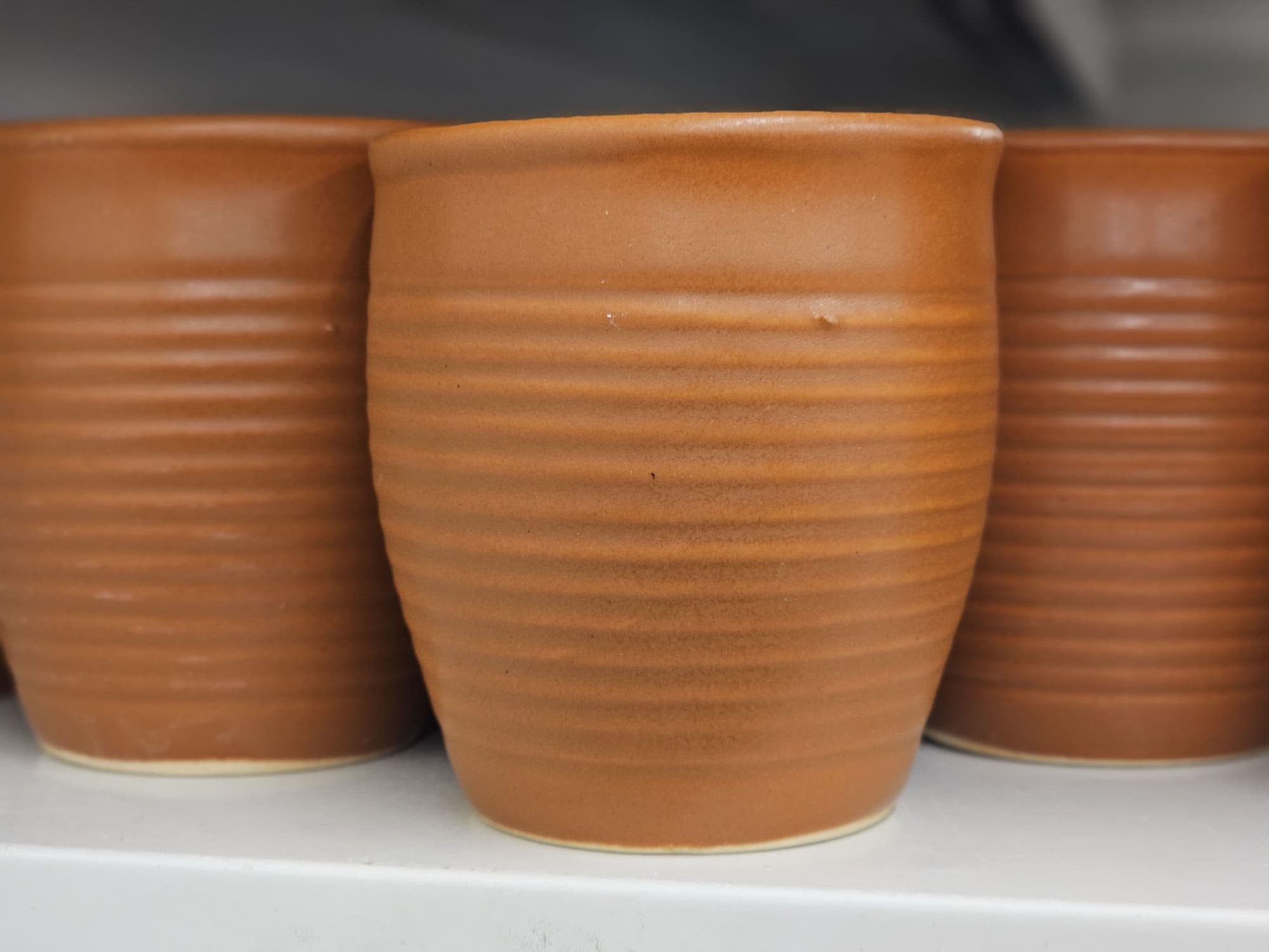 Tre bicchieri in terracotta con righe orizzontali lasciate dal tornio.