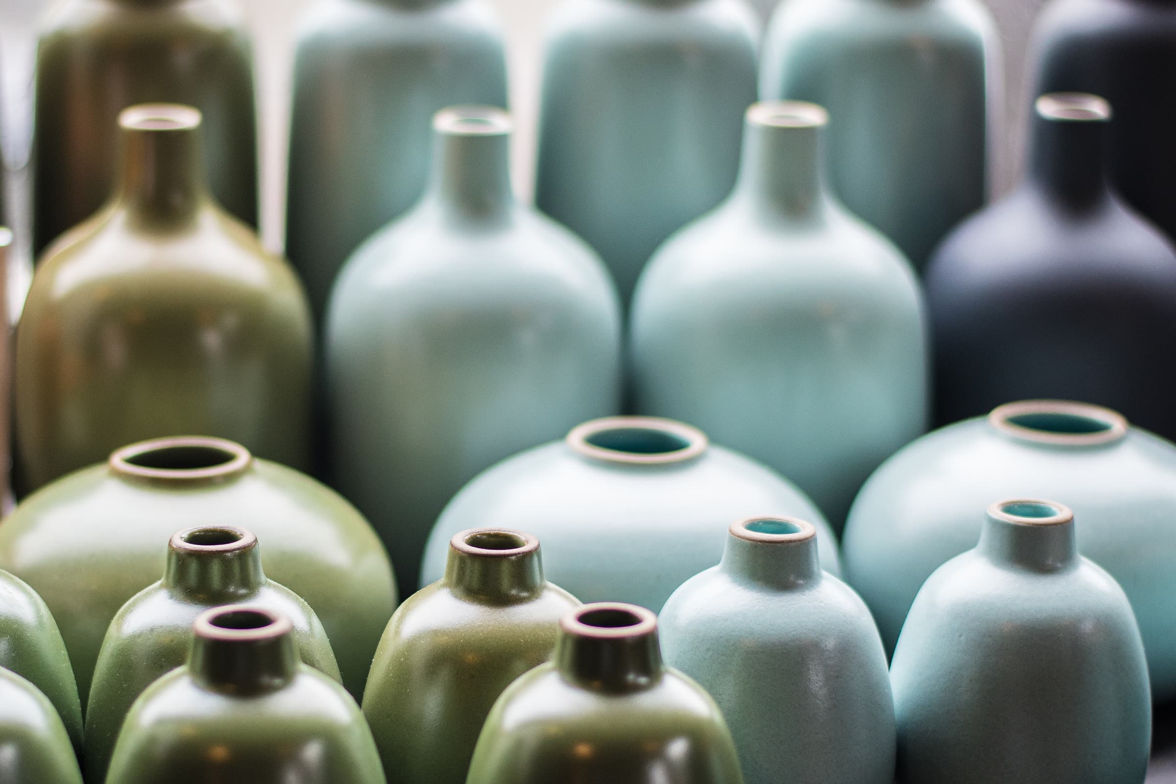 Una fila fitta di bottiglie in ceramica smaltate in verdi tenui, celadon e nero.