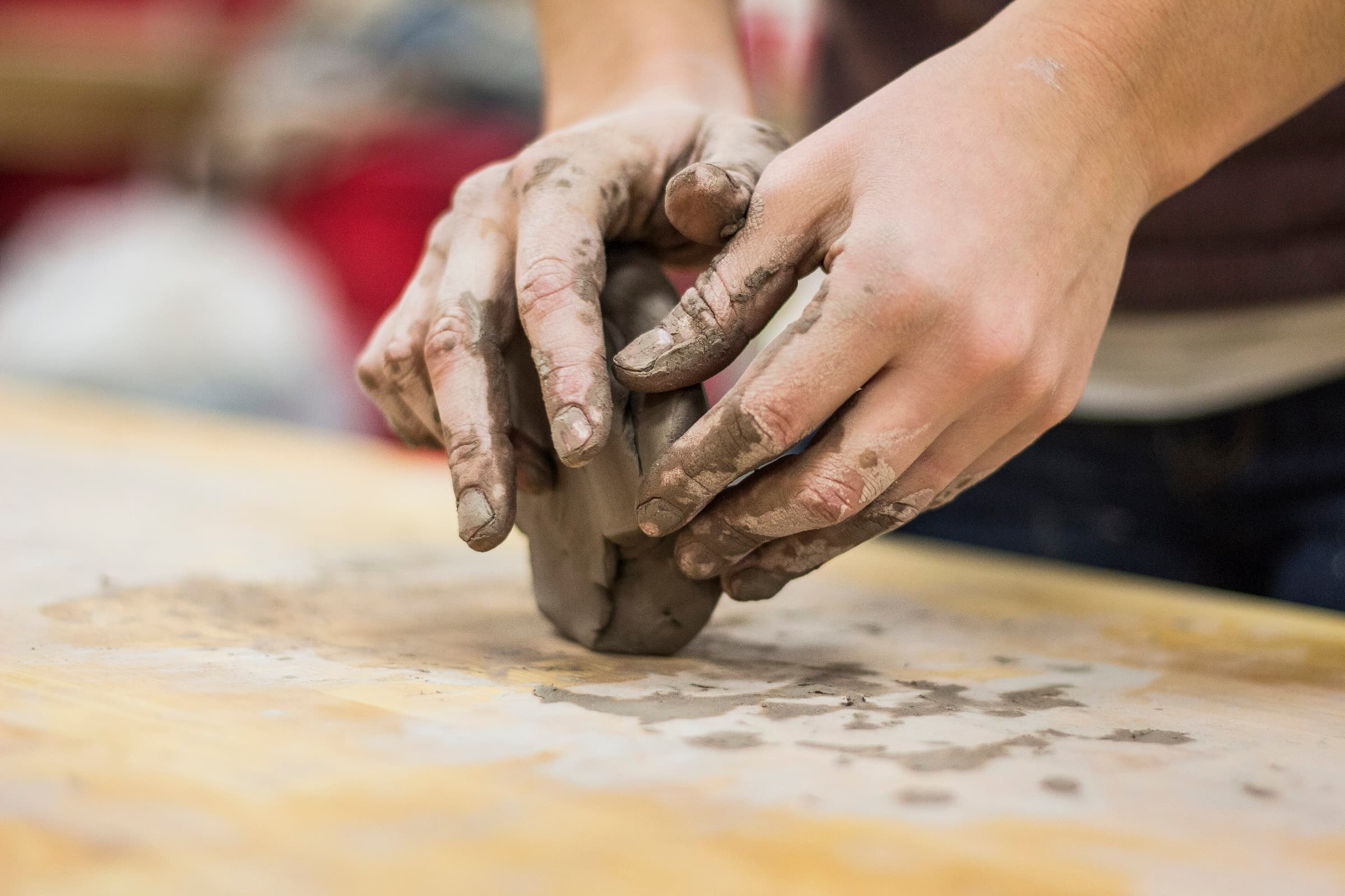 Due mani impastano un panetto d'argilla su un tavolo da lavoro.