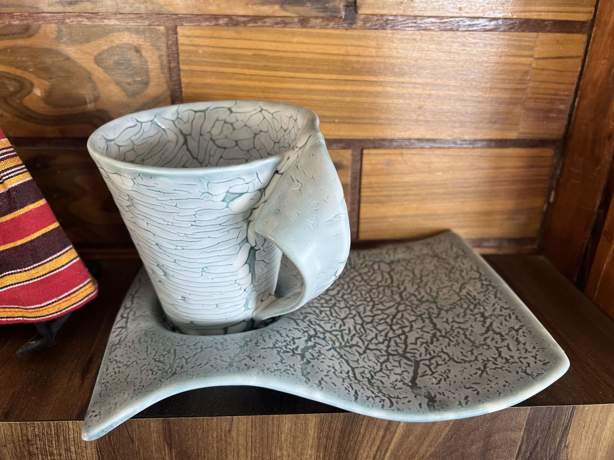 Tazza a cretto chiaro su un piattino ondulato con la stessa trama.