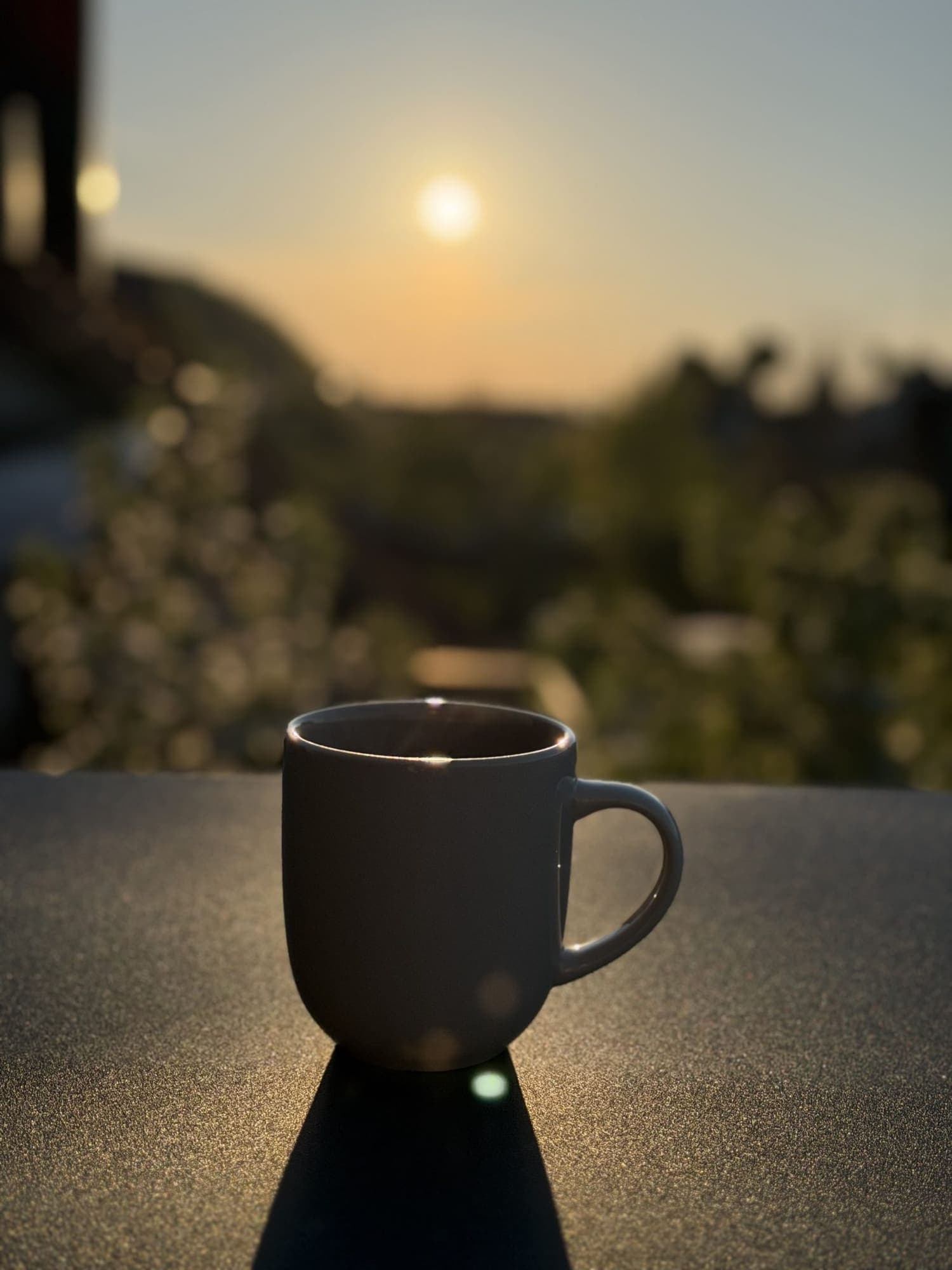 Tazza scura opaca appoggiata su un muretto al tramonto.