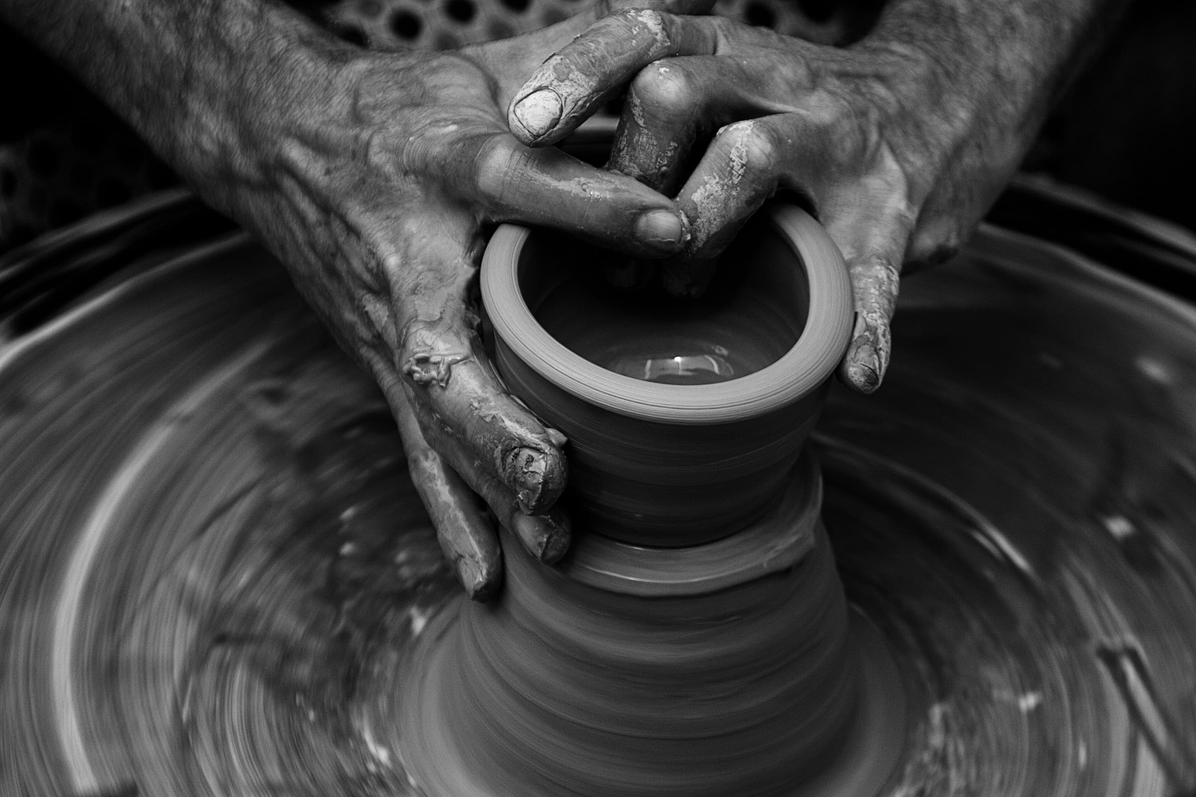 Foto in bianco e nero di mani che tirano su le pareti di un vaso sul tornio.
