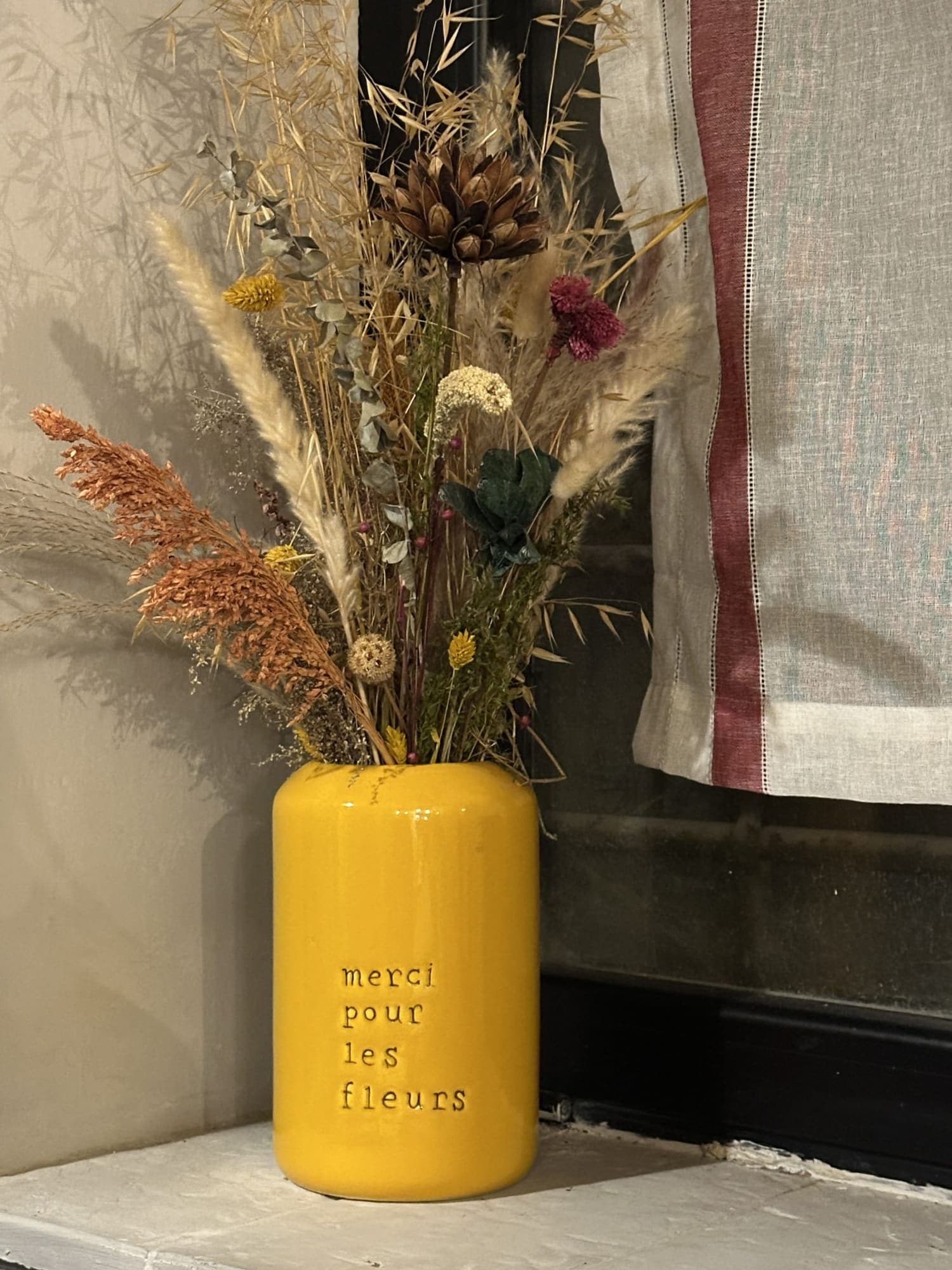 Vaso cilindrico giallo con un mazzo di fiori secchi.